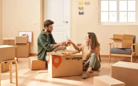 Un couple trinque avec des bouteilles devant une pizza, entouré de cartons. Un avis positif pour Movinga.