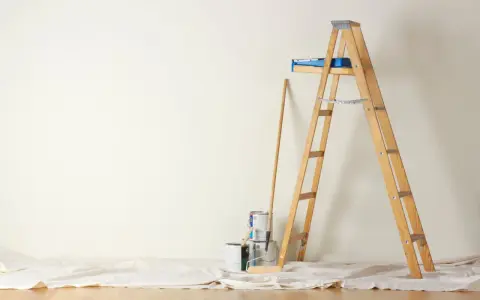 Préparation pour peindre une chambre : échelle en bois, pots de peinture, rouleau et bâton sur une toile de protection.