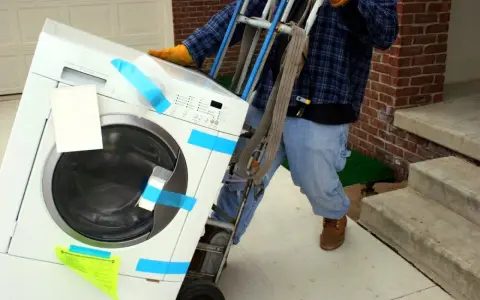 Un homme utilise un chariot pour comment monter une machine à laver dans les escaliers.