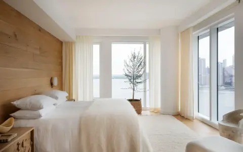 Une chambre à coucher simple et moderne avec un mur en bois, un lit blanc douillet et une vue imprenable sur la ville et l'eau.