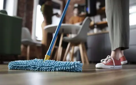 Nettoyage avant déménagement : une personne passe une serpillère bleue sur un parquet.