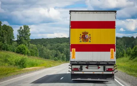 Camion aux couleurs de l'Espagne sur une route de campagne, prêt à déménager en Espagne. Paysage verdoyant sous un ciel nuageux.