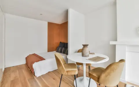 Idée pour aménager studio 30m2 en 2 pièces : un coin nuit cosy avec lit et tête de lit ocre, séparé par une table ronde et des fauteuils velours.