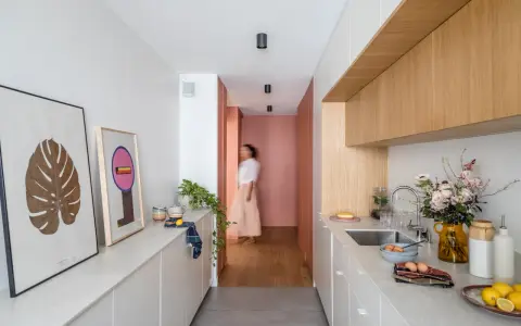 Cuisine moderne et lumineuse avec îlot central, décoration murale et personne marchant au fond.