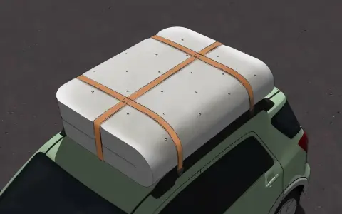 Un matelas est solidement attaché sur le toit d'une voiture verte, prêt pour le transport. Il montre comment rouler un matelas pour le transporter efficacement.
