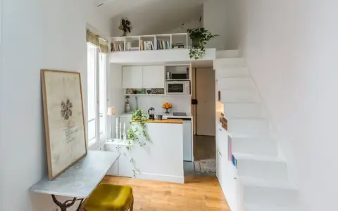 Un petit appartement optimisé avec une cuisine, un coin repas et un lit en mezzanine accessible par des escaliers blancs.