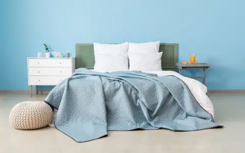 Une chambre paisible avec un lit douillet recouvert d'une couverture bleu glacier. Un pouf moelleux et une commode blanche complètent l'ensemble.