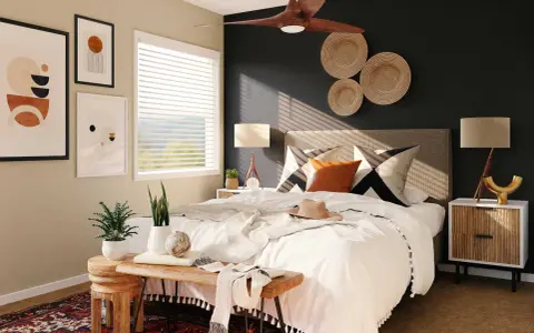 Une chambre moderne avec une décoration murale en vannerie, des tableaux abstraits et un ventilateur de plafond. Le lit est fait de blanc, avec des coussins graphiques et une touche de couleur ocre.