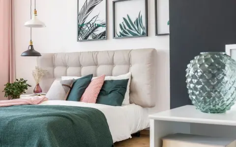 Une belle idée de tête de lit capitonnée, avec des coussins verts et roses, des plantes et des cadres botaniques.