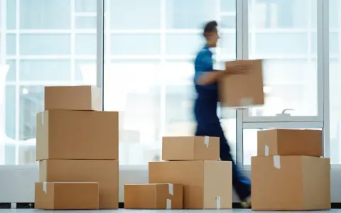 Un déménageur porte une boîte, entouré de cartons empilés. Une scène typique pour une facture déménagement.