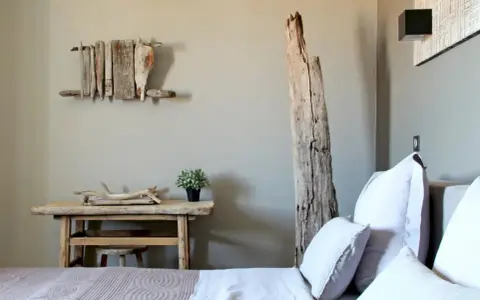 Idée pour comment décorer une chambre : un lit douillet, une table en bois brut, une plante verte et une sculpture murale en bois flotté.