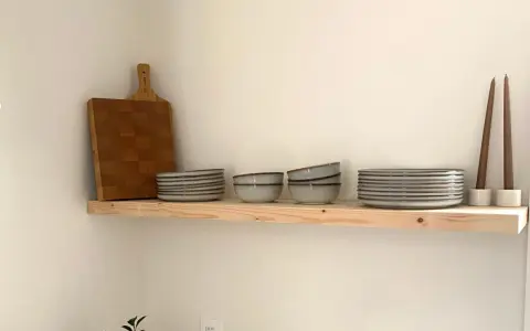 Étagère en bois brut, parfaite pour une cuisine de style **diy etagere bois**. Elle accueille une planche à découper, des assiettes, des bols et des bougies.