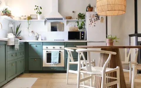 Cuisine verte avec four blanc, îlot central en bois et chaises blanches. Un modèle de cuisine simple et chaleureux.