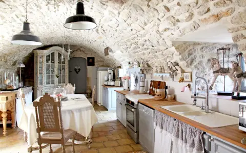 Cuisine rustique avec des vieux meubles patinés, un buffet ancien, une table dressée et des murs en pierre.