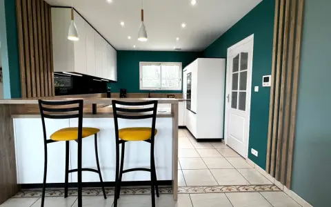 Cuisine moderne aux murs bleu canard, îlot central en bois, tabourets jaunes vifs. Une véritable inspiration cuisine pour des repas conviviaux.