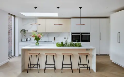 Élégante cuisine ouverte avec îlot central, tabourets en bois, et un jardin d'herbes aromatiques. Des armoires blanches et des fours intégrés complètent ce design moderne.