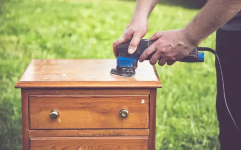 Préparation d'un meuble en bois : ponçage pour comment décaper un meuble en bois foncé. L'outil électrique enlève l'ancienne finition.
