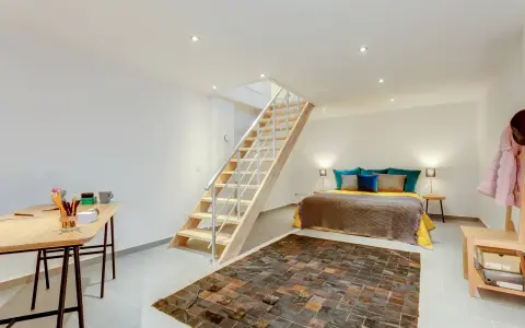 Aménager un sous-sol en pièce habitable : un lit douillet, un bureau fonctionnel et un escalier moderne créent un espace de vie confortable.