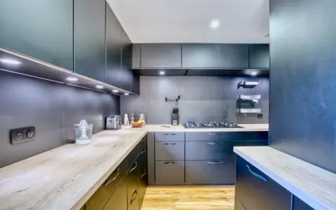 Cuisine moderne aux armoires sombres et plans de travail en bois. Une plaque de cuisson est installée, créant une cuisine sans hotte visible.