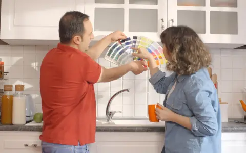 Un couple choisit des couleurs pour peindre le carrelage de sa cuisine, tenant un éventail de nuanciers.