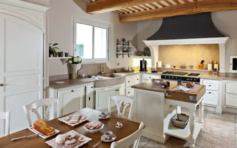 Cuisine de maison provençale avec poutres apparentes, évier en pierre, et table dressée pour un goûter gourmand.