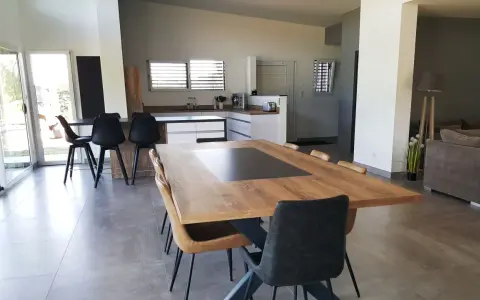 Grande cuisine ouverte sur salon, avec îlot central, table en bois et chaises modernes.