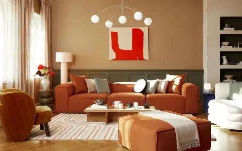 Salon chaleureux avec canapé orange, fauteuil assorti et tapis graphique. Un excellent conseil couleur peinture pour une ambiance cosy.