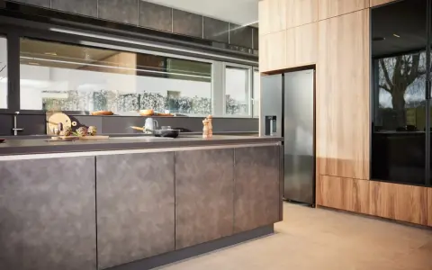 Une cuisine en plan moderne avec des armoires en bois et des surfaces sombres. Un réfrigérateur en acier inoxydable est visible.