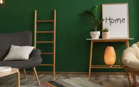 Un salon cosy avec un mur vert sapin, un fauteuil gris, une échelle en bois, une plante et un cadre "Home".