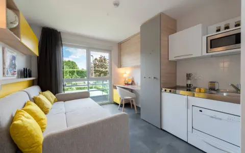 Aménagement studio moderne avec canapé, coin cuisine, bureau et vue sur jardin.