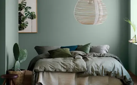 Une chambre vert sauge apaisante avec un lit douillet, un cactus et une œuvre d'art botanique.