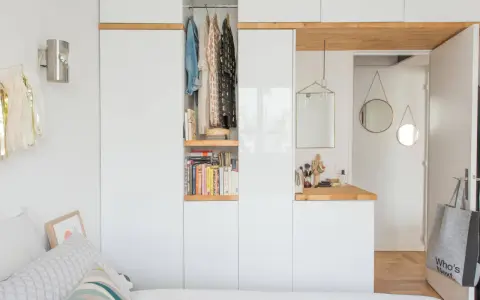Chambre avec dressing intégré, organisée avec des étagères de livres et des vêtements suspendus. Un coin coiffeuse avec miroir et accessoires complète l'espace.