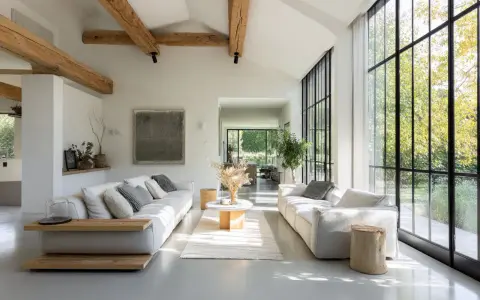 Salon lumineux avec poutres apparentes, rappelant l'esprit d'une maison hangar. Deux canapés blancs font face à une grande baie vitrée.