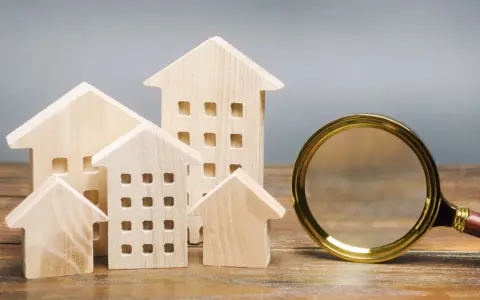 Maquettes de maisons en bois et une loupe, symbolisant la recherche pour trouver un logement rapidement.