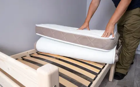 Un homme montre comment plier un matelas sur un sommier en bois.