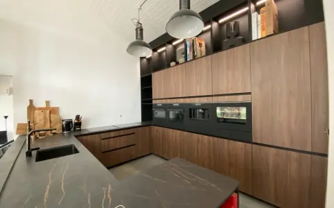 Cuisine moderne avec îlot central, plan de travail en marbre noir veiné, meubles en bois, électroménagers intégrés. L'implantation cuisine est pensée pour l'efficacité.