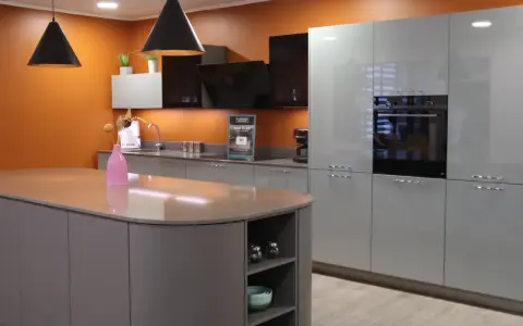 Un exemple de cuisine moderne aux lignes épurées, avec un îlot central gris et des meubles hauts gris clair. L'orange vif du mur apporte une touche de dynamisme.