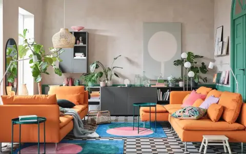 Deux canapés orange vif dans un salon moderne avec des plantes, un tapis coloré et un mur vert.