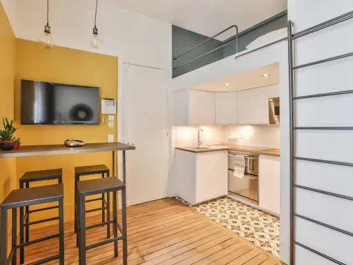 Aménagement studio 18m² : cuisine moderne, coin repas jaune vif avec TV, et lit mezzanine accessible par une échelle.