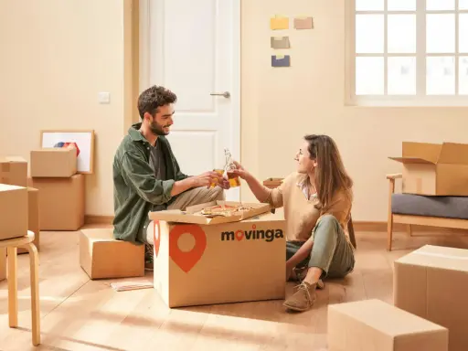 Un couple trinque avec des bouteilles devant une pizza, entouré de cartons. Un avis positif pour Movinga.