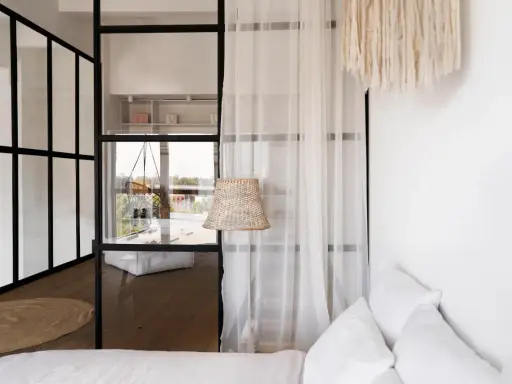 Verrière noire séparant une chambre en deux, avec une seule fenêtre visible. Un rideau blanc et un abat-jour en rotin ajoutent une touche cosy.