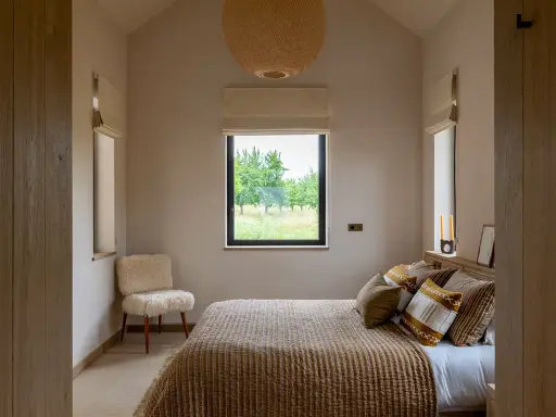 Aménagement petite chambre cosy avec lit douillet, fauteuil mouton et vue sur la nature.