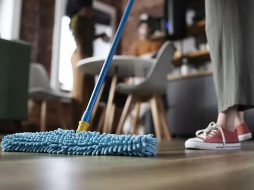 Nettoyage avant déménagement : une personne passe une serpillère bleue sur un parquet.