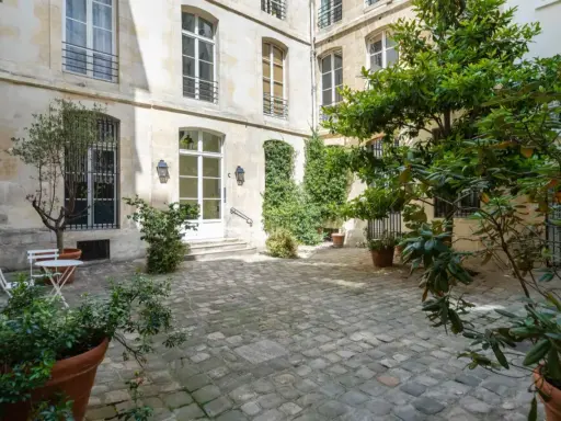 Cour pavée d'un immeuble parisien, avec un petit olivier et une table. Idéal pour un projet de déménager à Paris et profiter de la douceur de vivre.