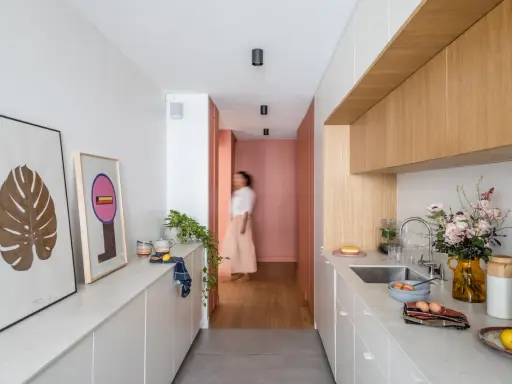 Cuisine moderne et lumineuse avec îlot central, décoration murale et personne marchant au fond.