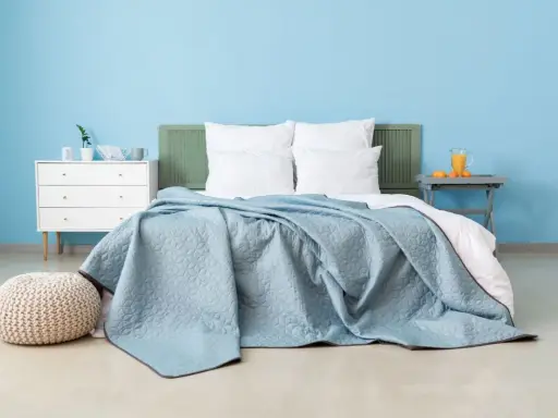 Une chambre paisible avec un lit douillet recouvert d'une couverture bleu glacier. Un pouf moelleux et une commode blanche complètent l'ensemble.