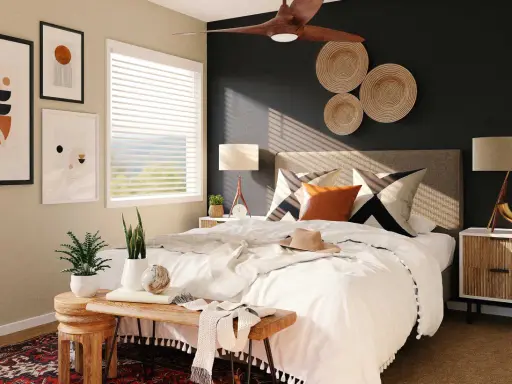 Une chambre moderne avec une décoration murale en vannerie, des tableaux abstraits et un ventilateur de plafond. Le lit est fait de blanc, avec des coussins graphiques et une touche de couleur ocre.