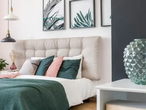Une belle idée de tête de lit capitonnée, avec des coussins verts et roses, des plantes et des cadres botaniques.