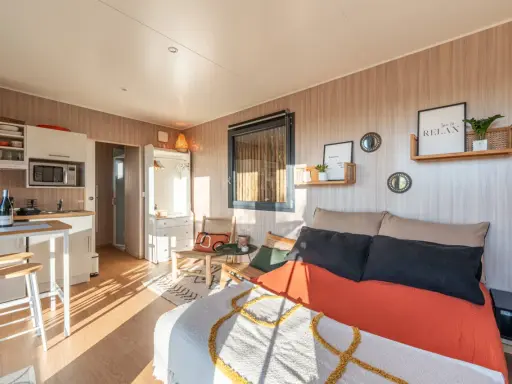 Aménagement d'un plan studio 20m2 en longueur : coin cuisine, lit confortable, fauteuils en rotin et décoration murale zen.