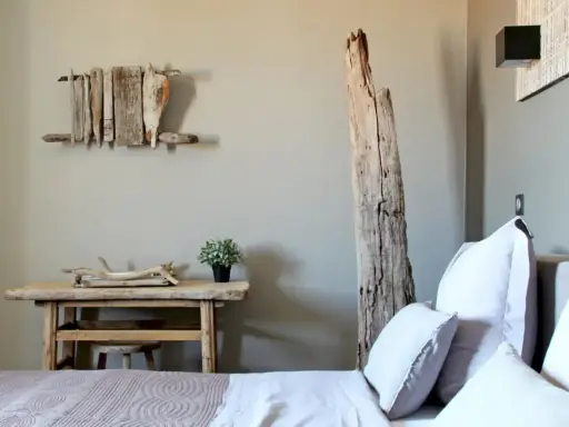 Idée pour comment décorer une chambre : un lit douillet, une table en bois brut, une plante verte et une sculpture murale en bois flotté.